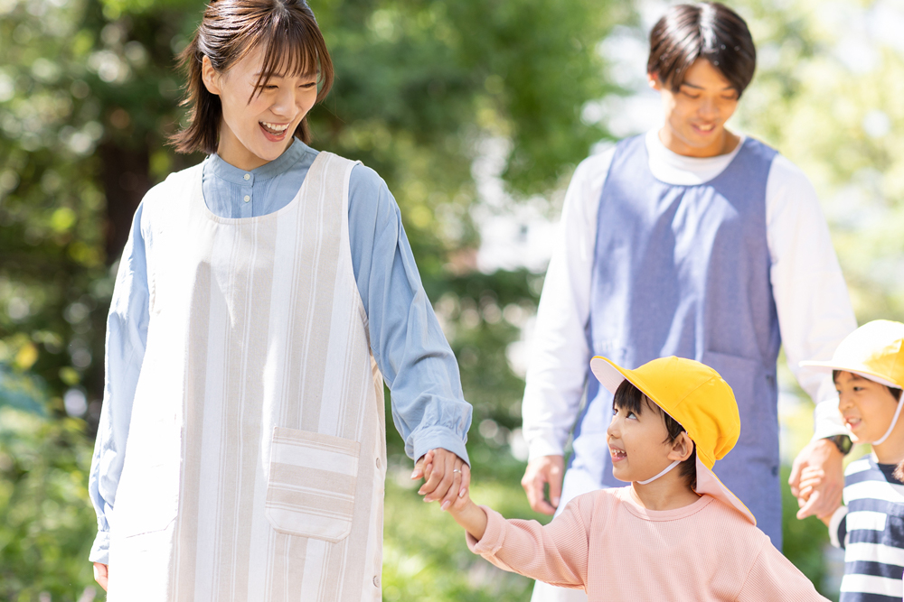 保育士と笑顔で手をつないでいる園児